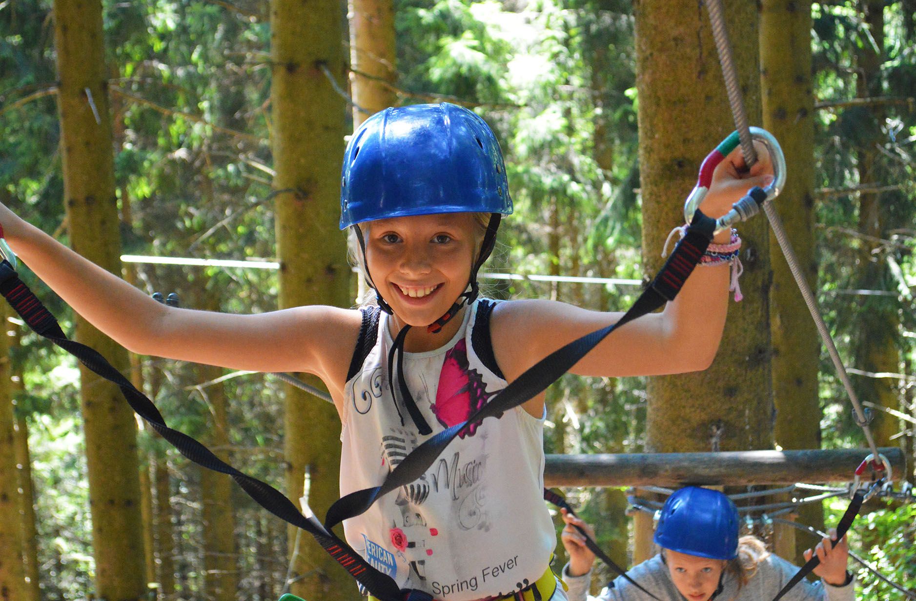 A girl in a blue helmet balances on a climbing course in the forest.