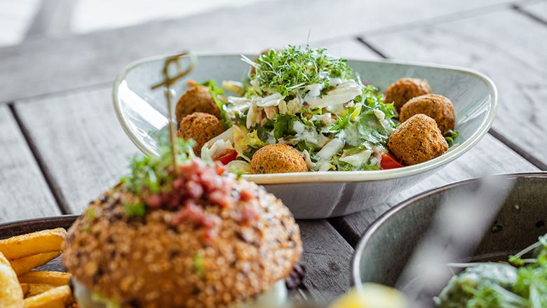 A deep plate with salad and falafel, a burger in the foreground.