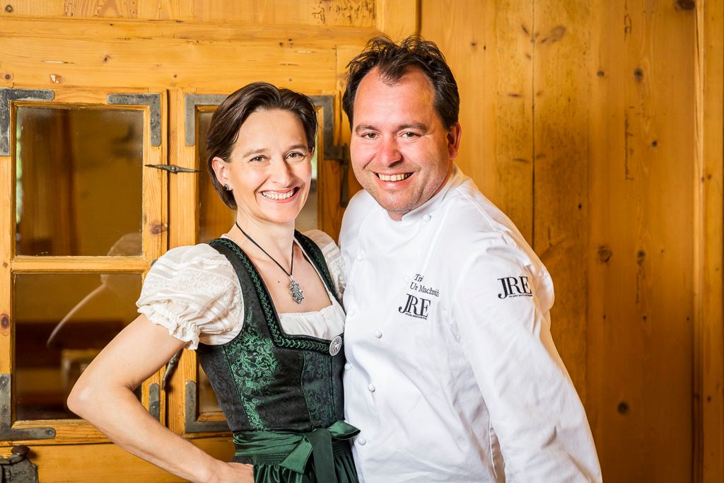 A man in a chef's jacket and a woman in traditional costume smile at the camera.