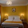 Elegant hotel room with yellow walls, double bed, chandelier and picture on the wall.