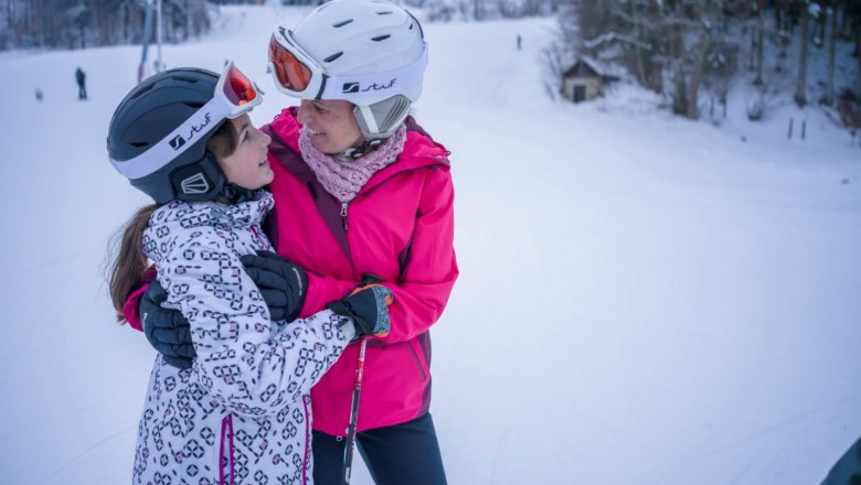 Two people in ski equipment embrace on a ski slope.