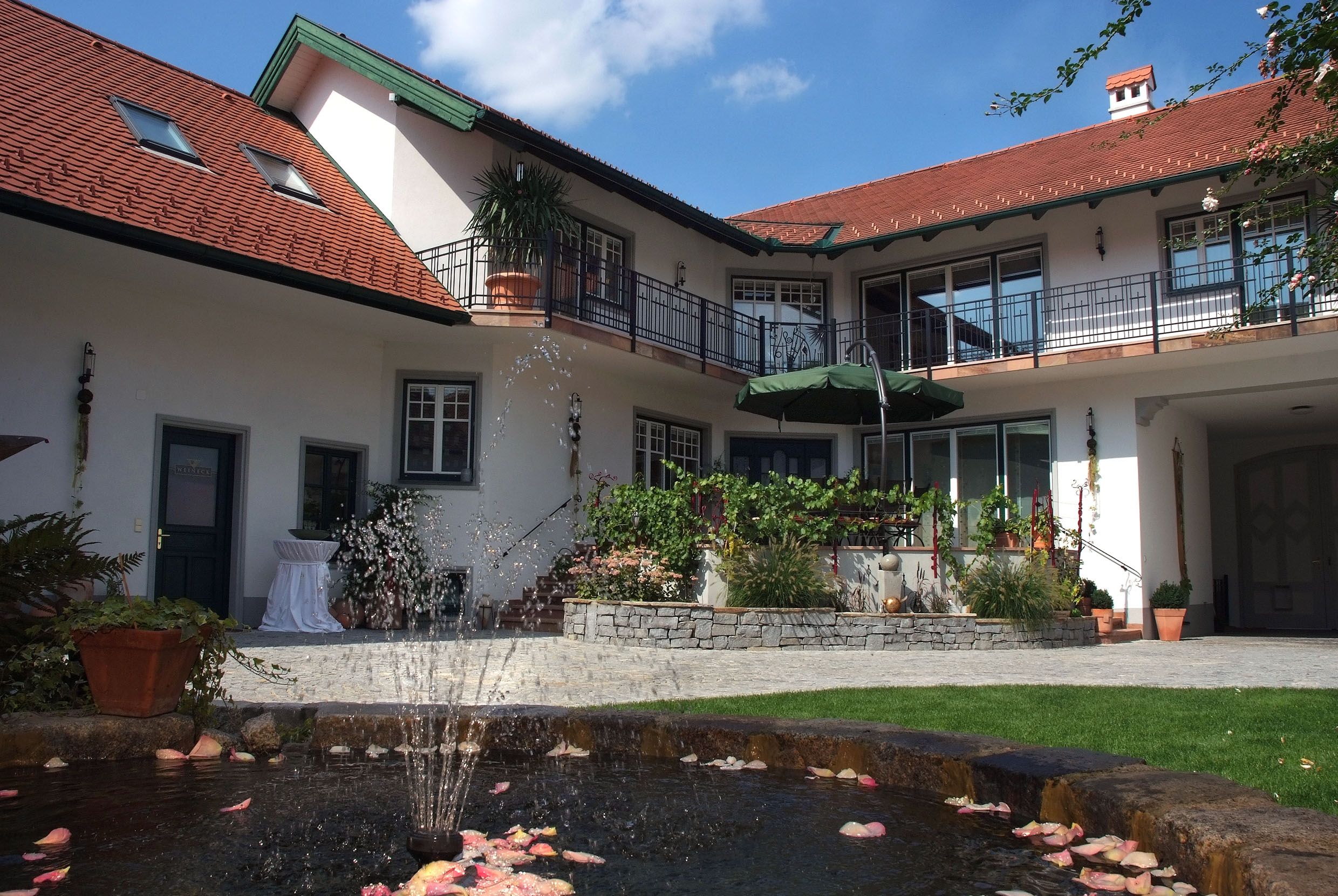 An inner courtyard with a fountain, surrounded by a two-storey building with red roofs and balconies.