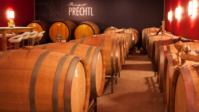 Wine cellar with wooden barrels and table with chairs, Prechtl winery.
