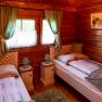 Cozy bedroom with wooden walls, two single beds, green curtains and bedside tables with lamps.