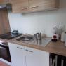 Modern kitchenette with stove, sink, coffee machine, toaster and kettle.