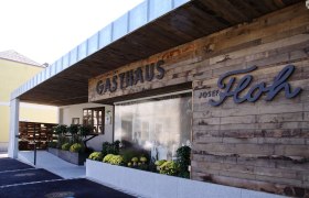 Exterior view of the Josef Floh guesthouse with wooden wall and plants.