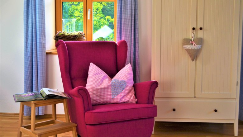 Cozy room with pink armchair, cushions, small table and wardrobe.