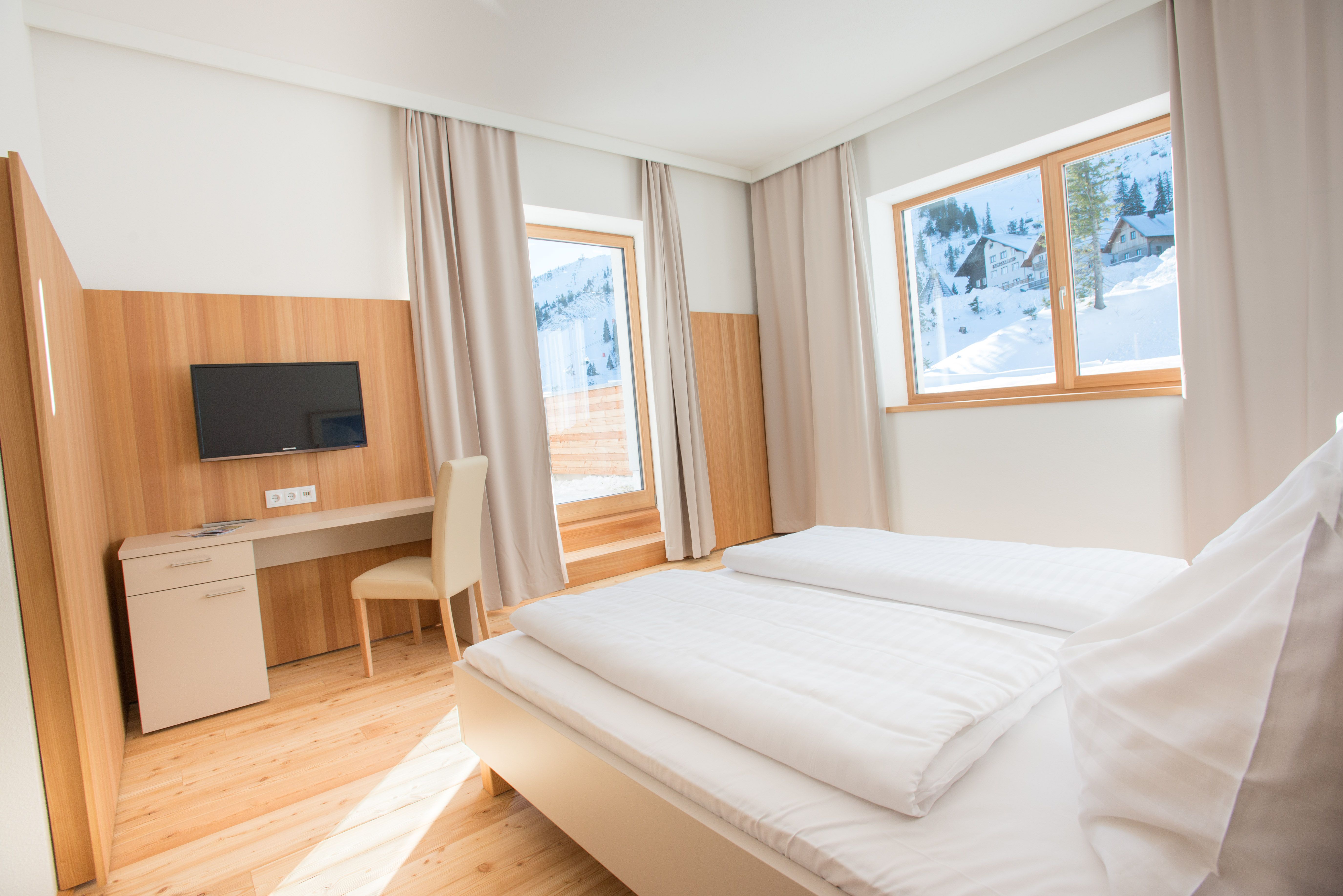 Bright hotel room with double bed, desk and view of snow-covered mountains.