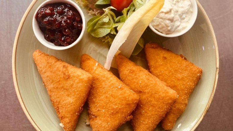 A plate with breaded cheese, salad, cranberries and a white sauce.