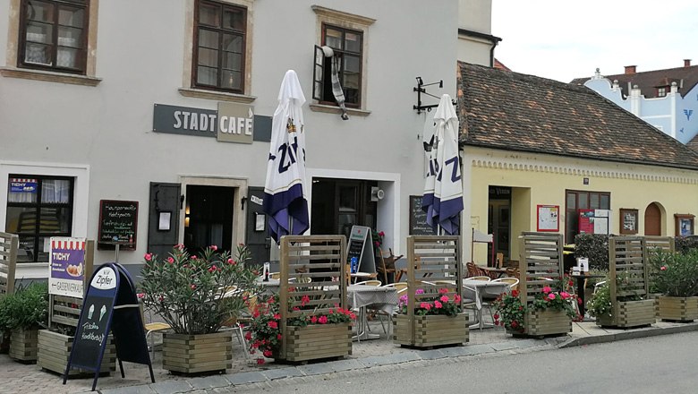 Exterior view of a café with tables, chairs and parasols in front of the building.