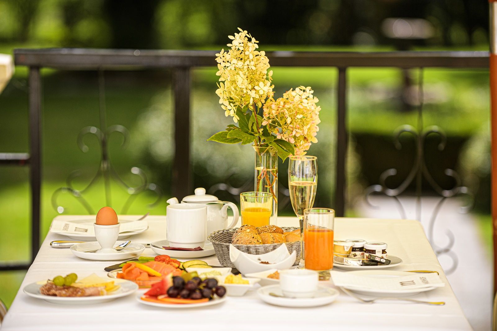 Breakfast table on the terrace with flowers, juice, bread rolls and eggs.