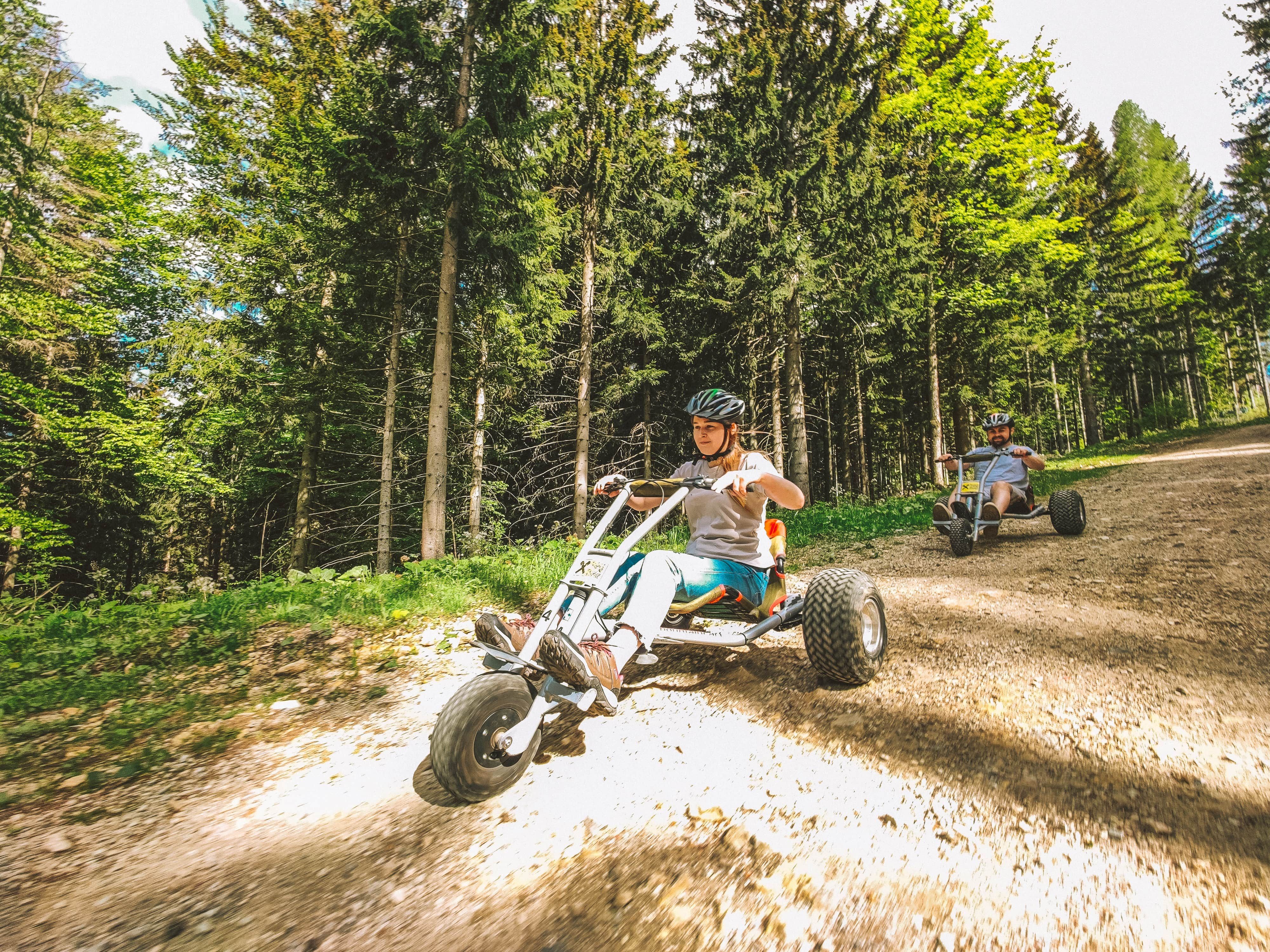 Two people are riding mountain carts on a forest path.