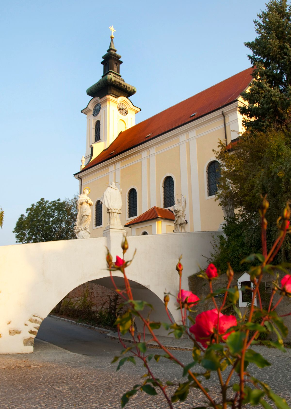Wolkersdorf parish church with statues and roses in the foreground.