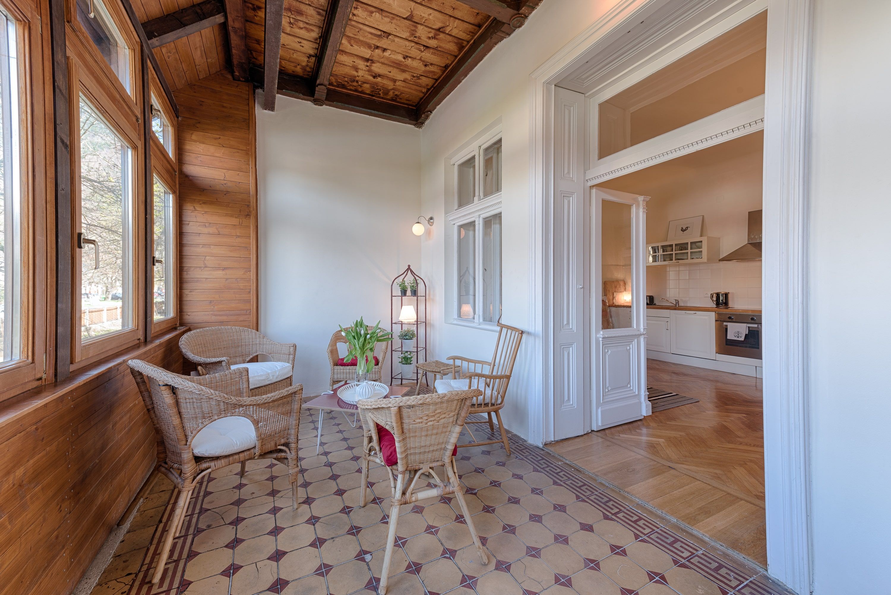 Conservatory with wooden walls, rattan furniture and view into a kitchen.