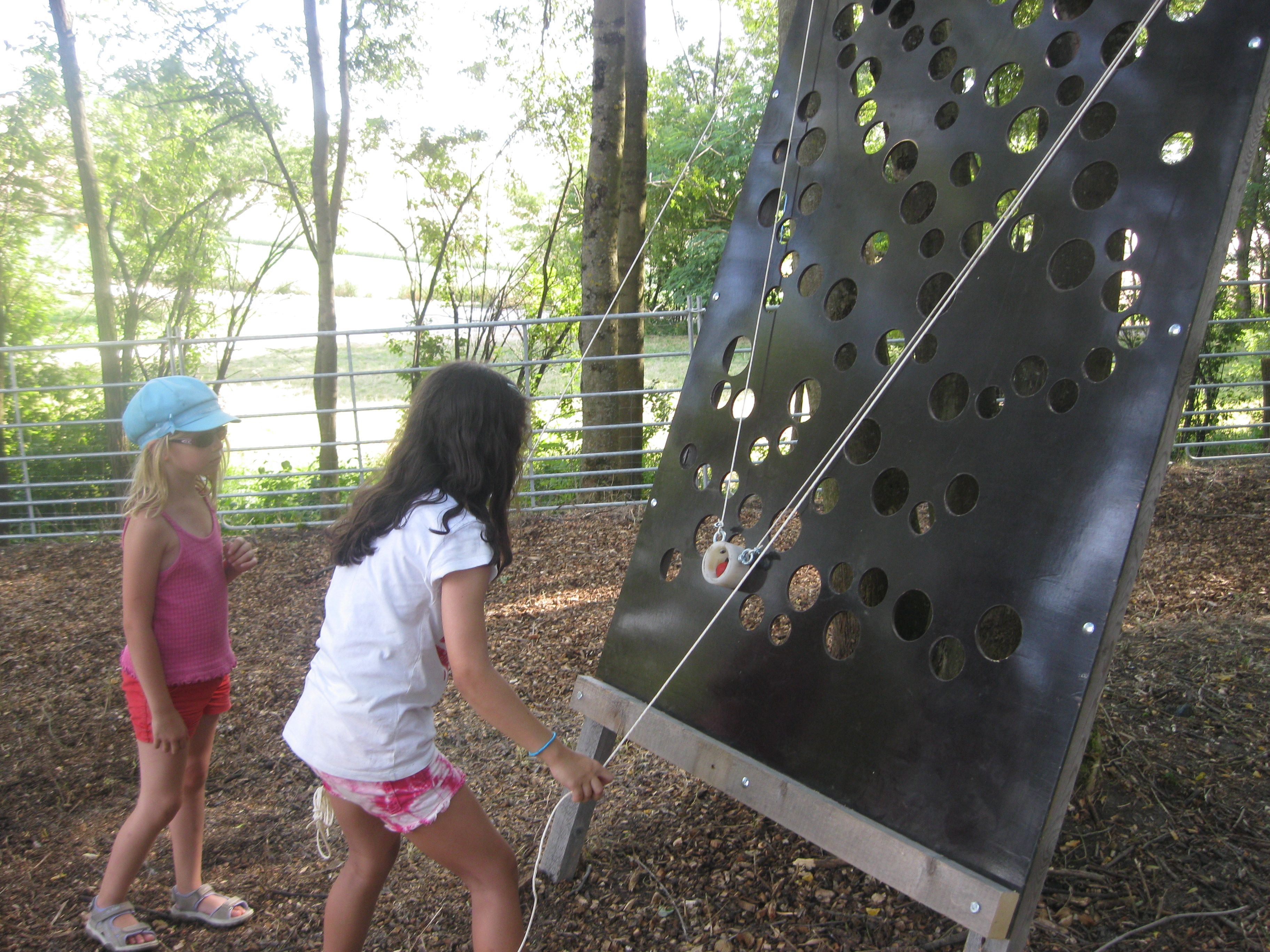 Two children playing on a perforated wall outdoors.