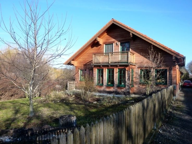Wooden house with balcony and garden, surrounded by a wooden fence.