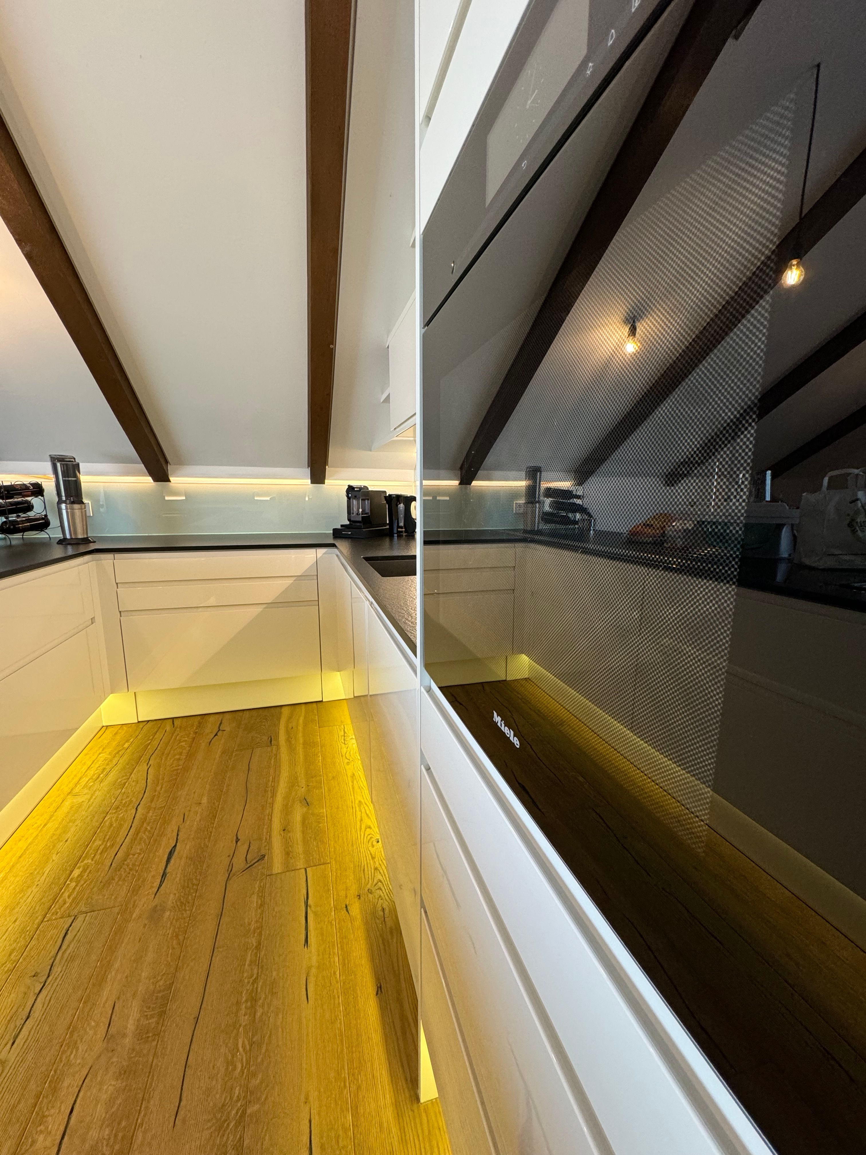 Modern kitchen with wooden floor, white cupboards and built-in oven.