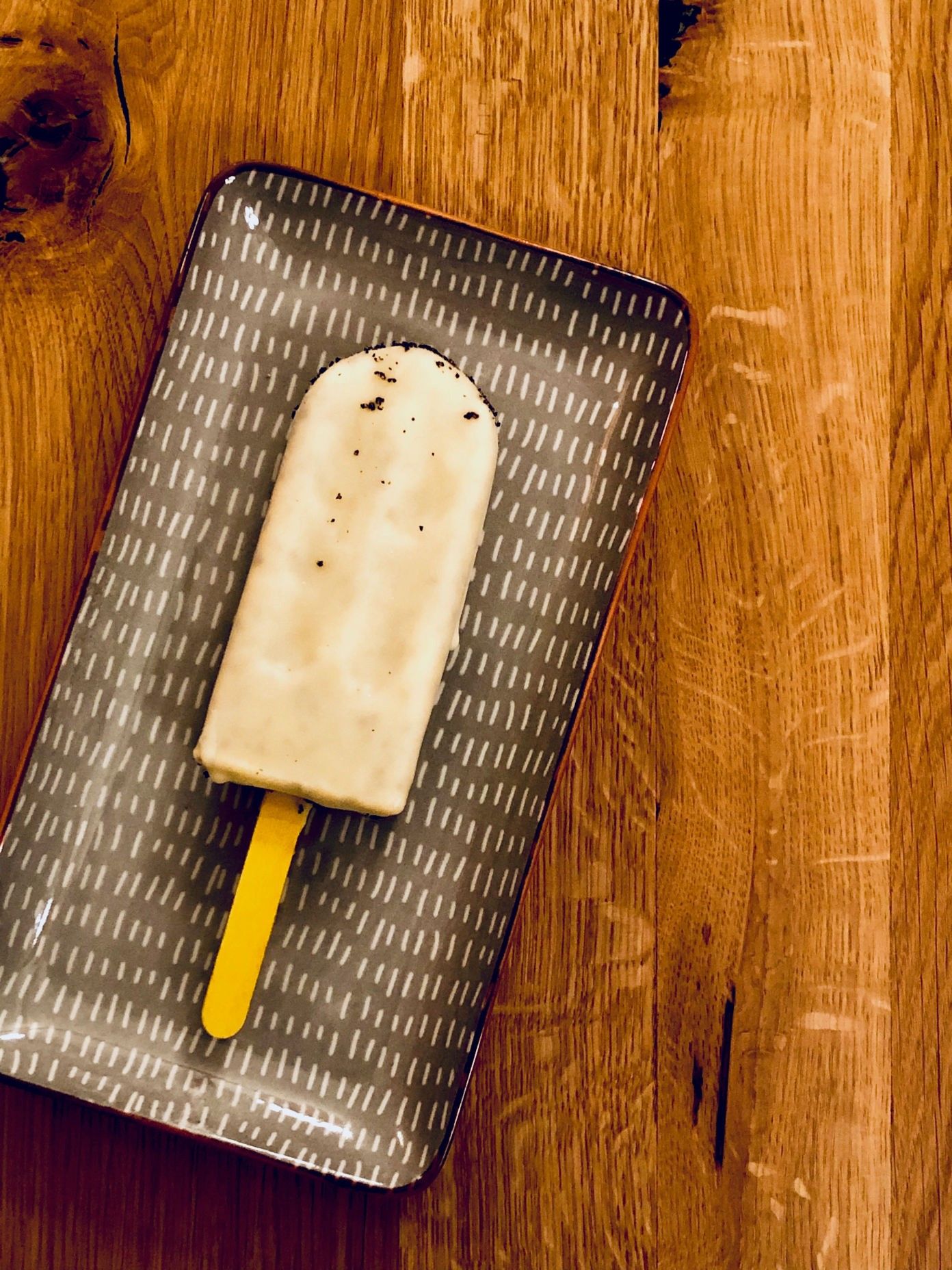 A popsicle on a patterned plate on a wooden table.