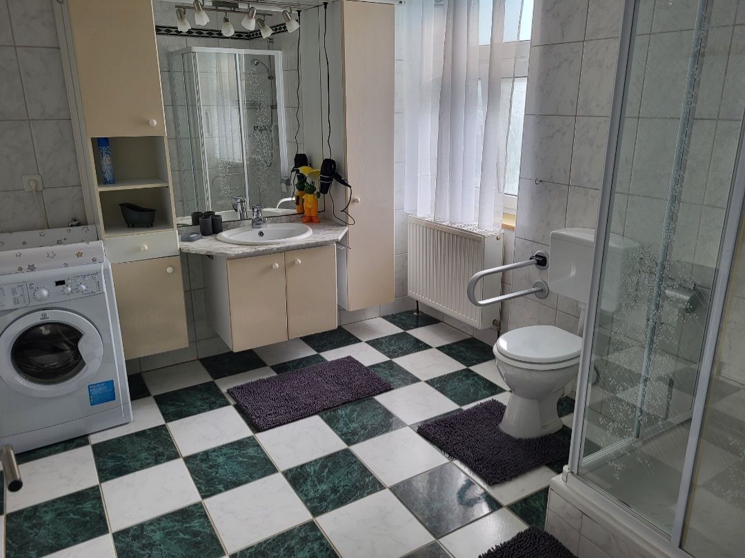Bathroom with washing machine, shower, toilet and washbasin. Checkerboard tiles and white curtains.