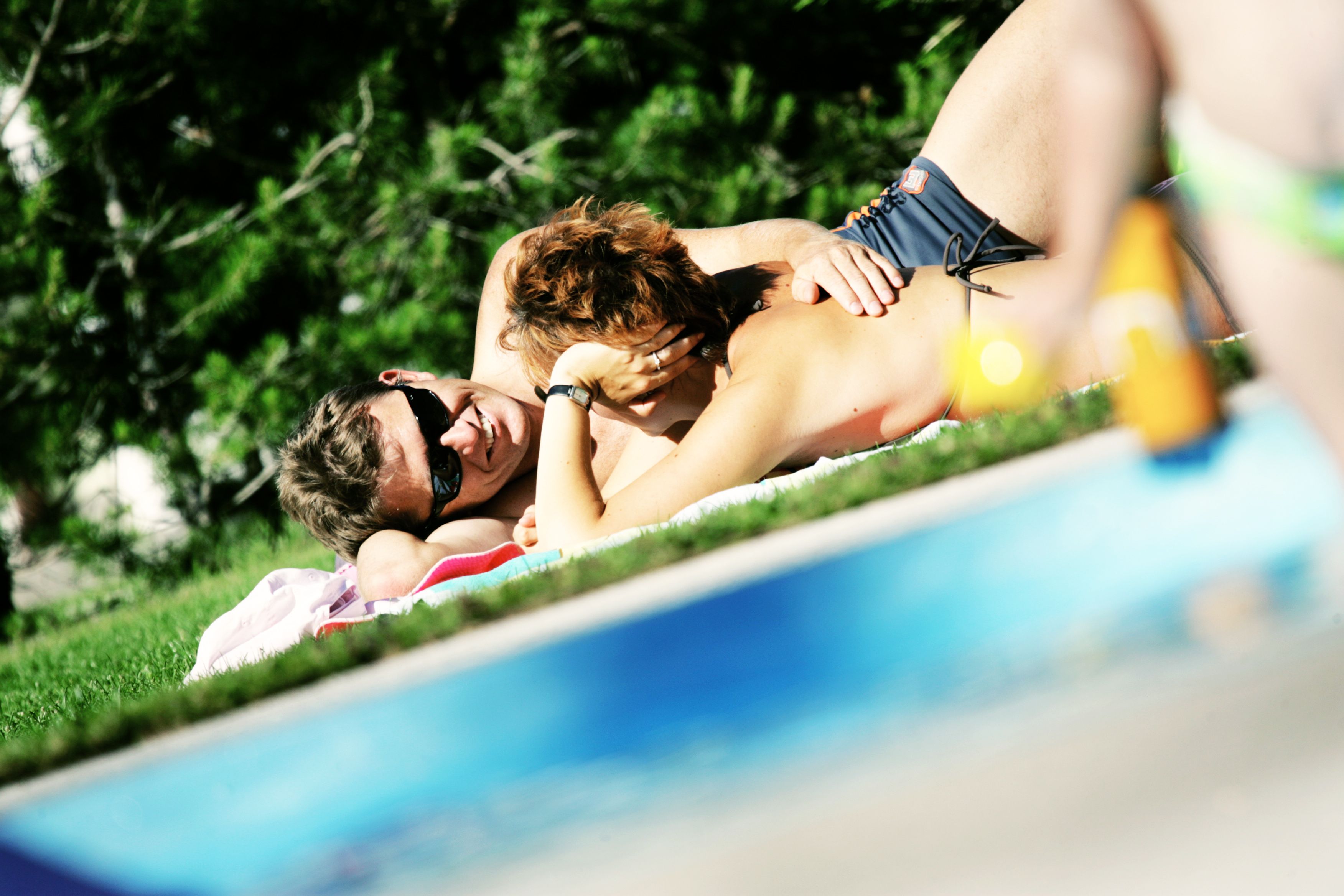 A couple is relaxing on a lawn next to a pool.