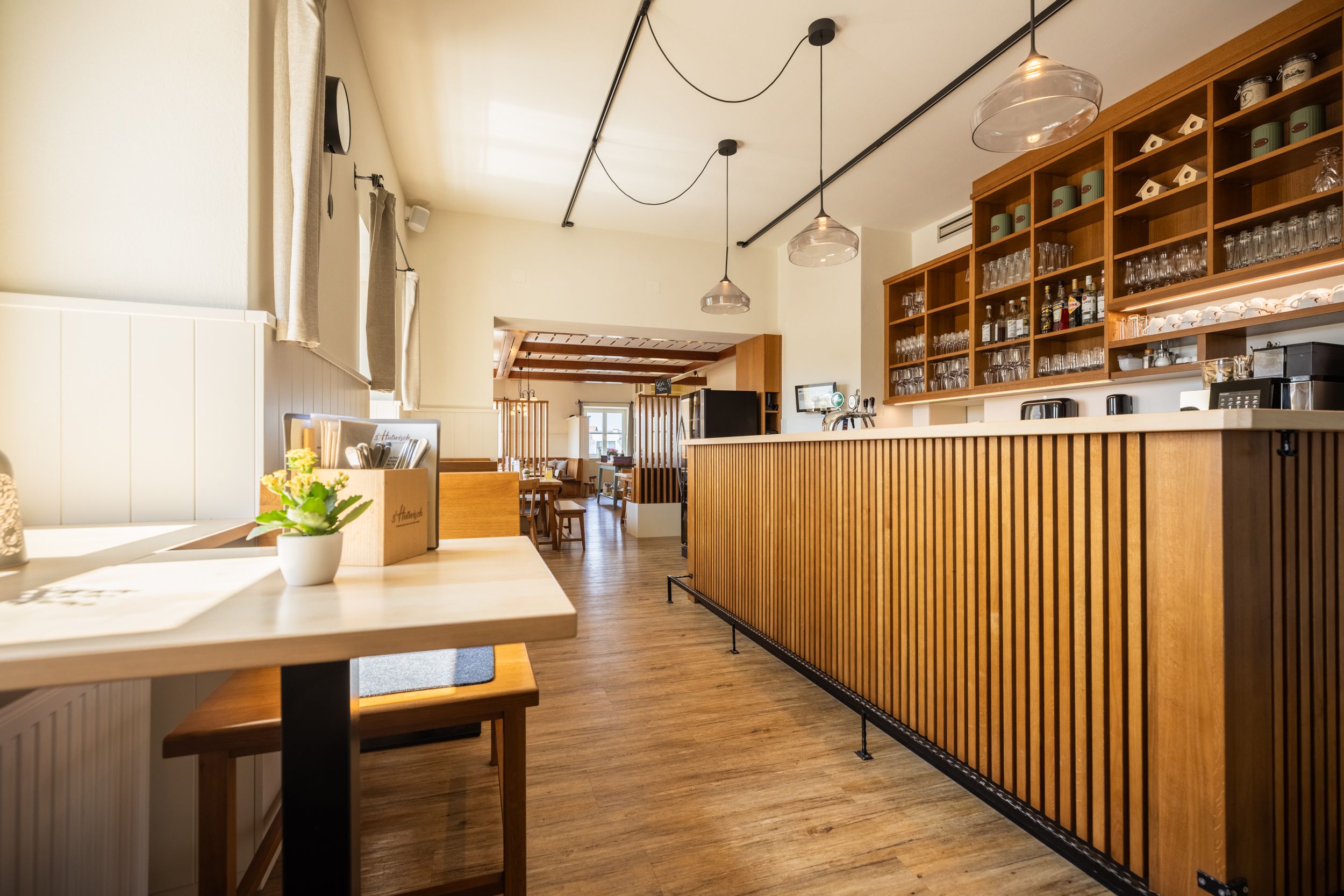 Interior view of a modern restaurant with wooden furniture and counter, lots of light comes in through the windows, modern lamps hang above the bar.
