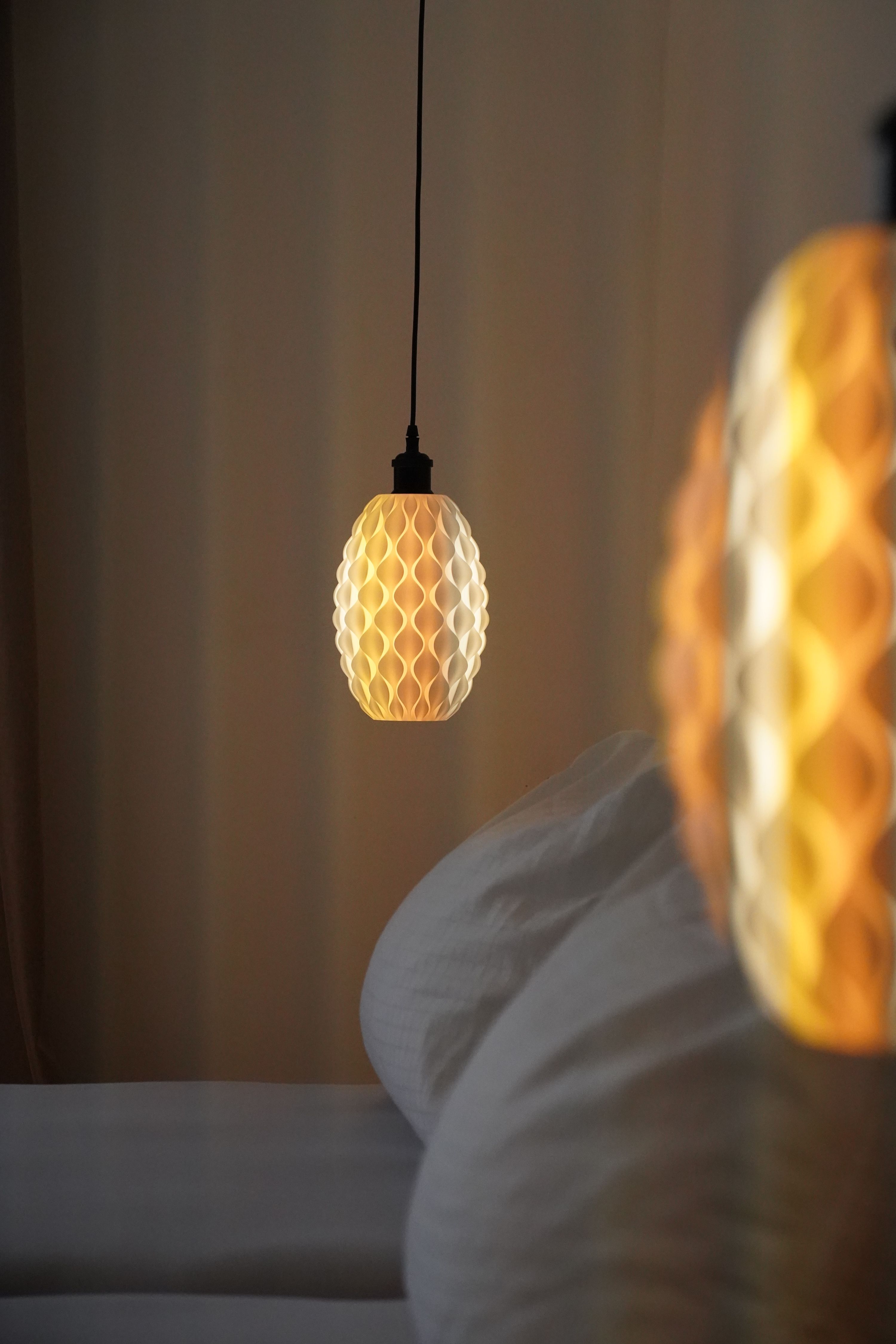 Close-up of a hanging lamp with a honeycomb pattern emitting warm light, next to a bed.