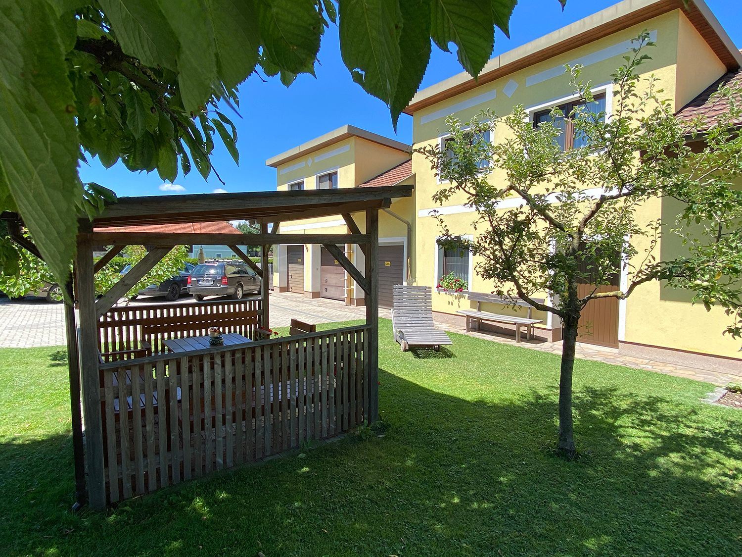 Garden with pavilion, yellow house and car in the background.