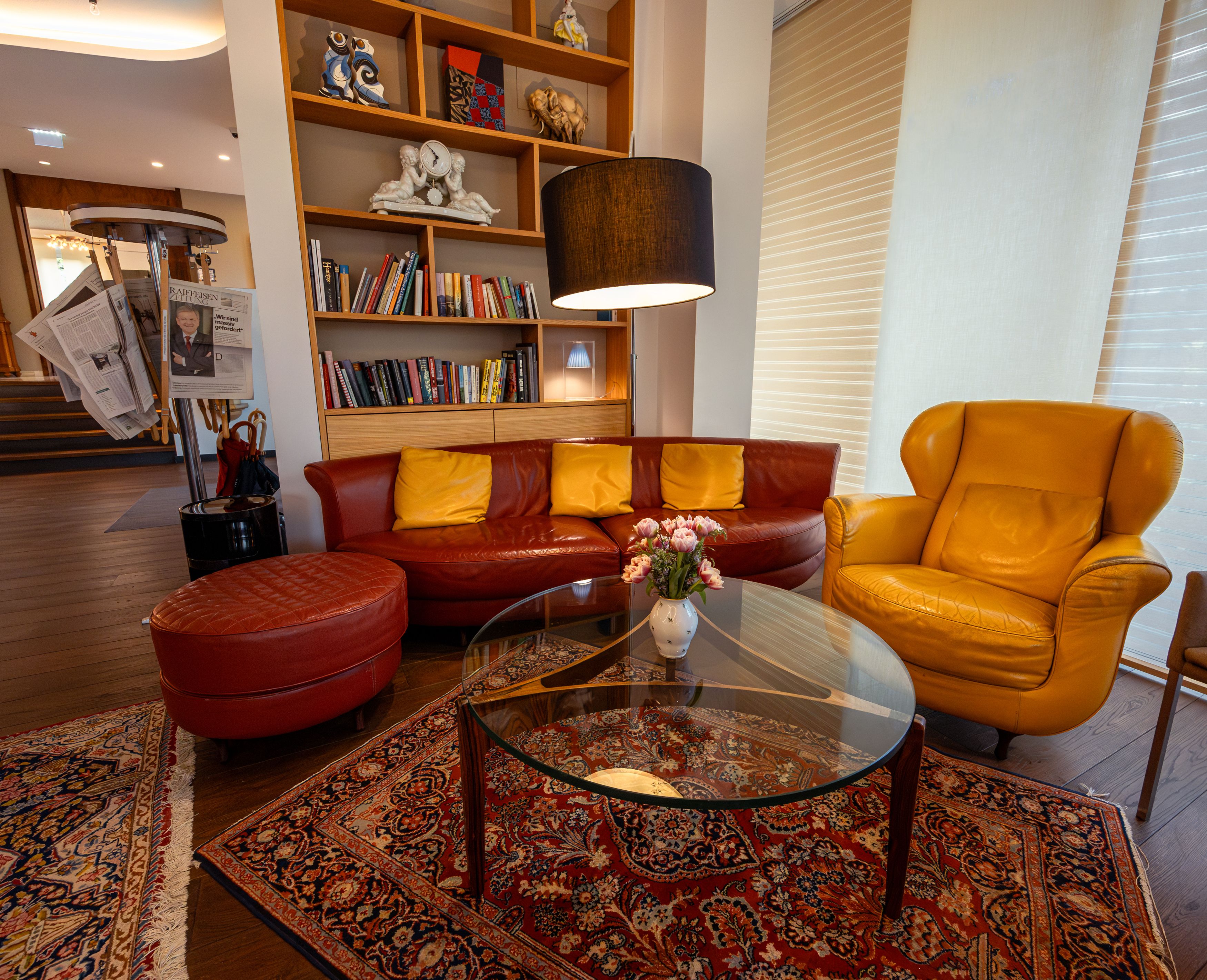 Cozy hotel lobby with red and yellow leather furniture, bookshelf and newspaper rack.