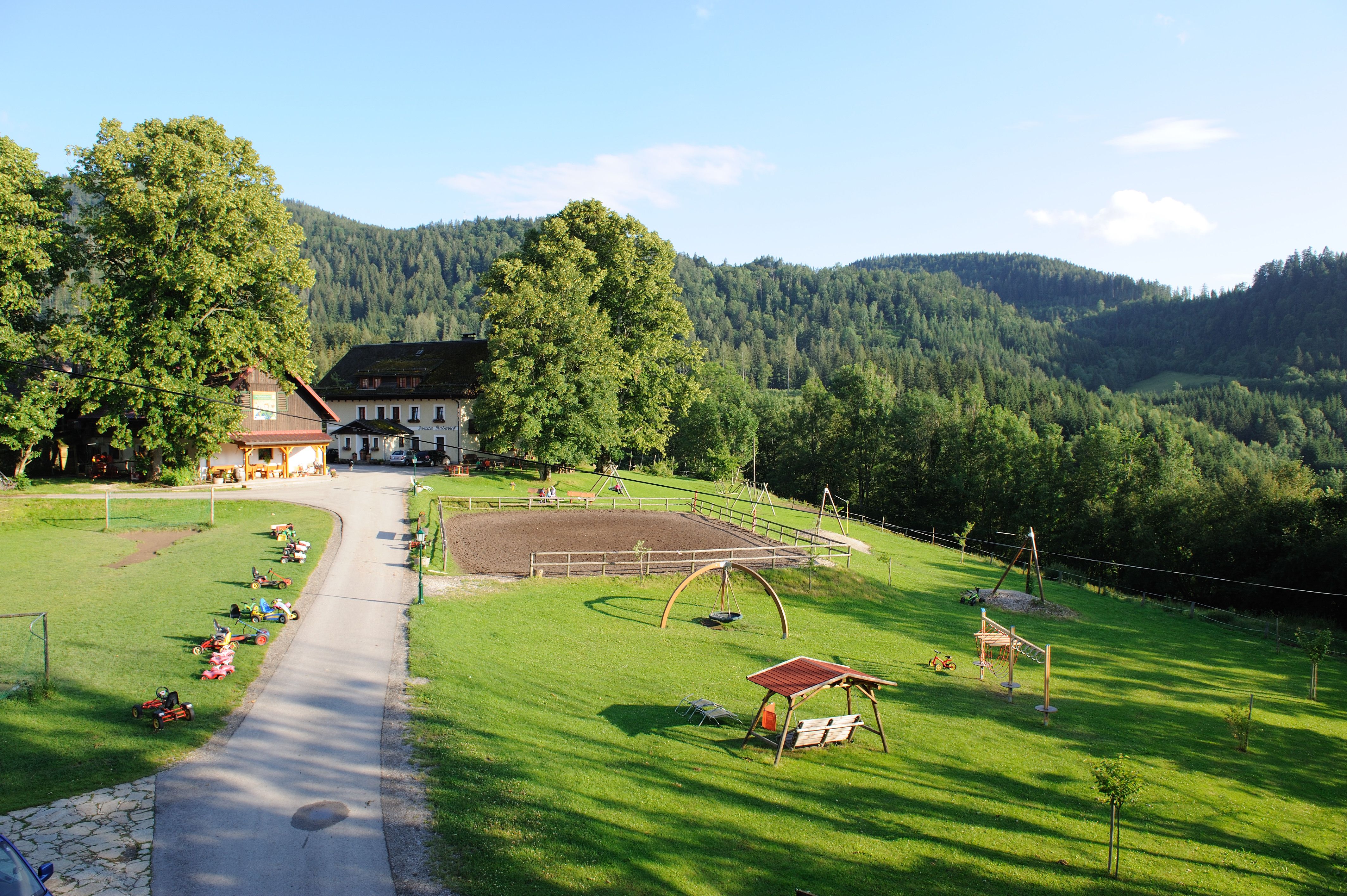 A farm in a green, hilly landscape with a playground and Kettcars on a meadow.