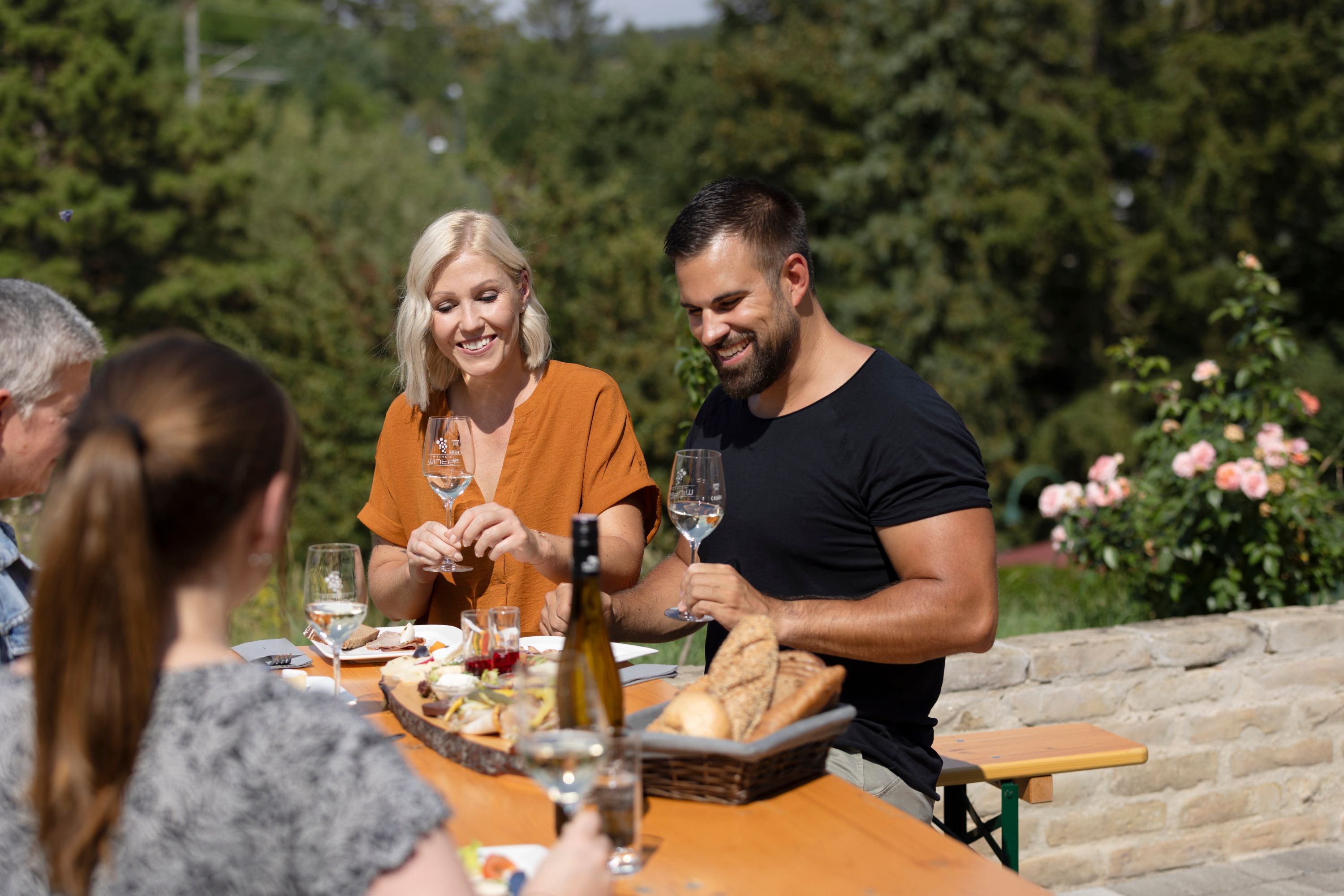 Group of people sitting at an outdoor table enjoying wine and bread.