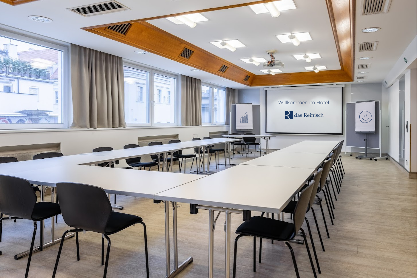 Seminar room at Das Reinisch Hotel with tables, chairs and presentation screen.