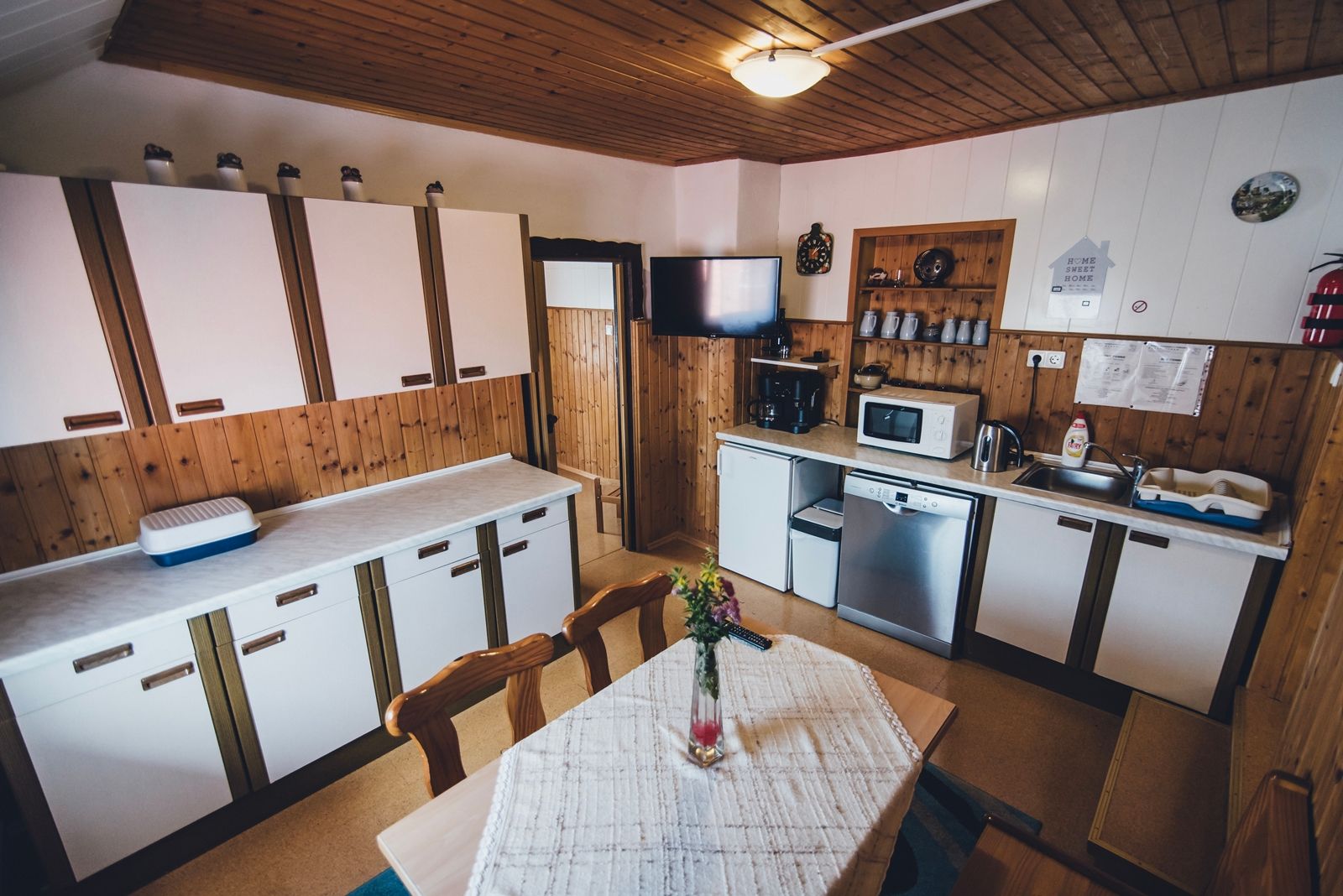 Cozy kitchen with wooden walls, white cabinets, dining table and modern appliances such as microwave and dishwasher.