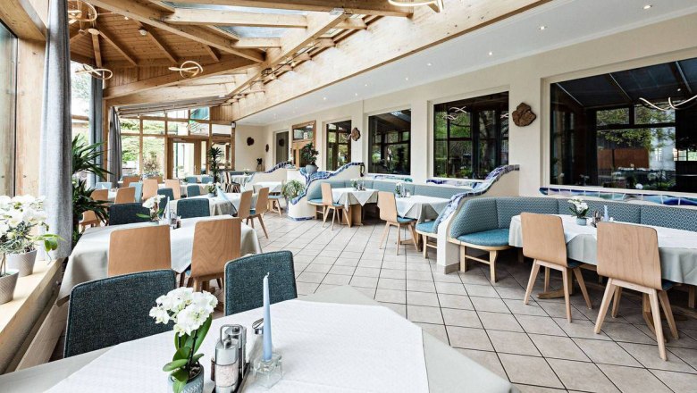 A bright conservatory with laid tables and wooden furniture.