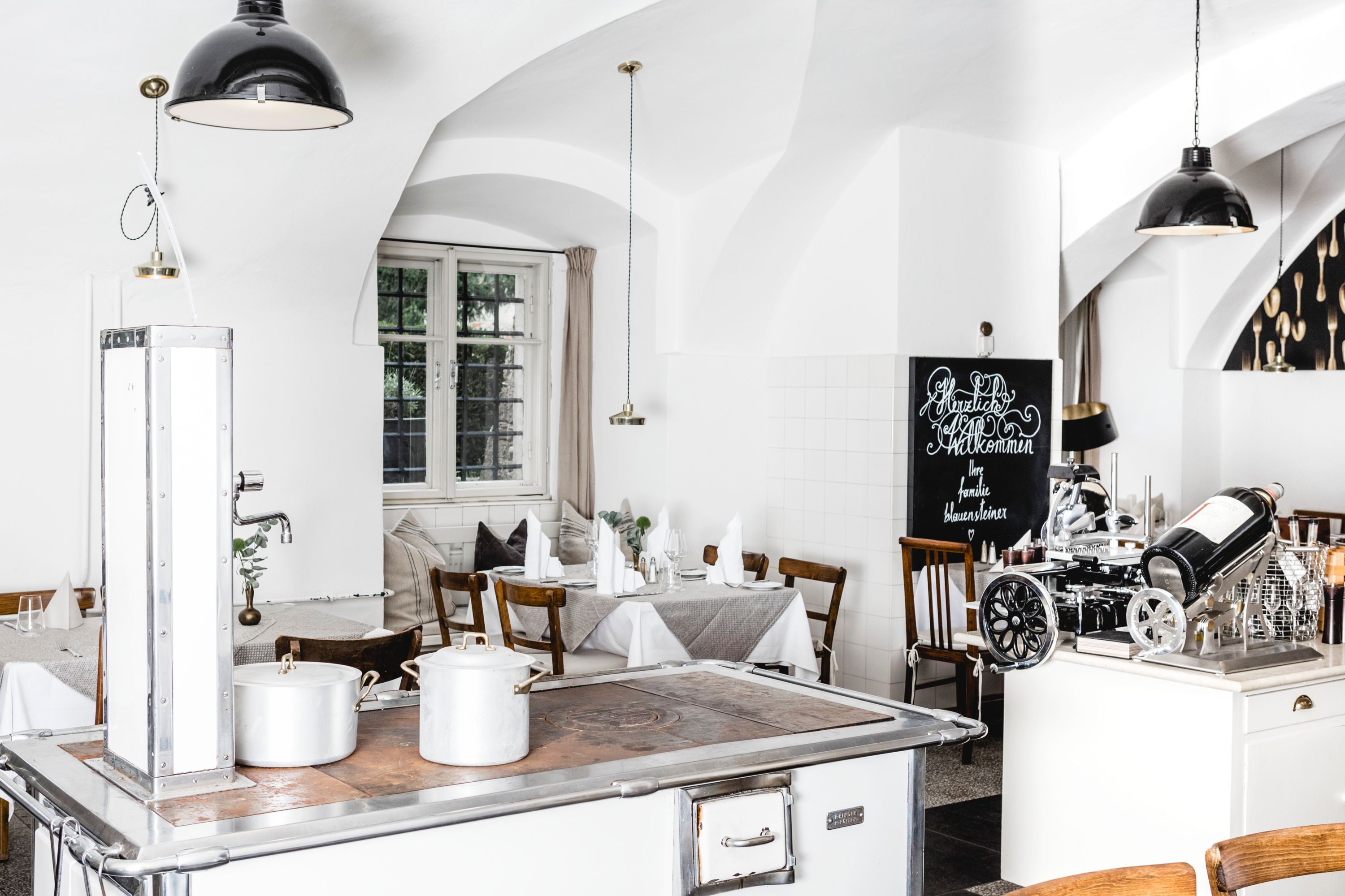 Bright restaurant interior with white walls, wooden furniture and an old stove.