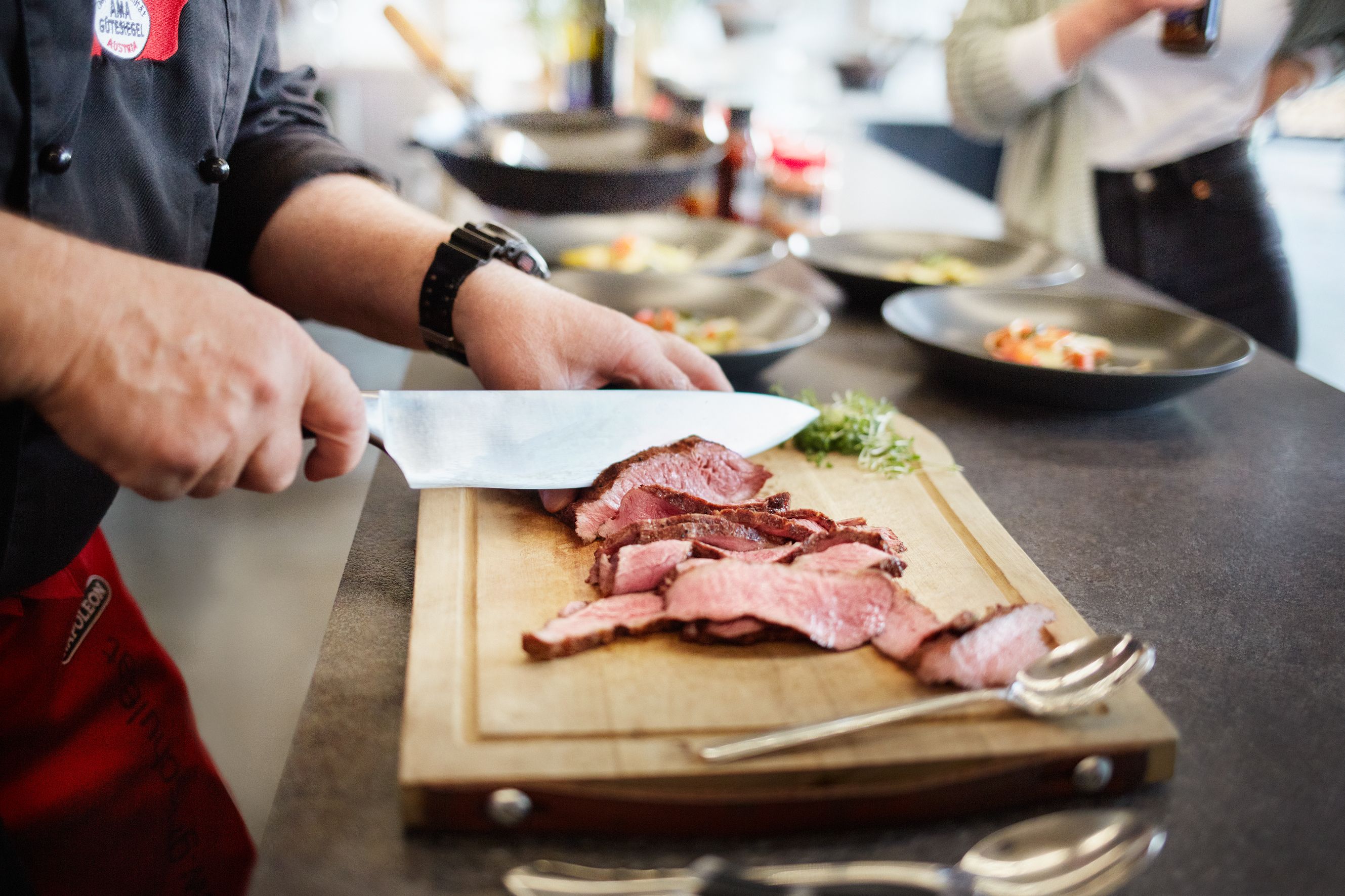 A grill master cuts meat on a wooden board in a show kitchen.