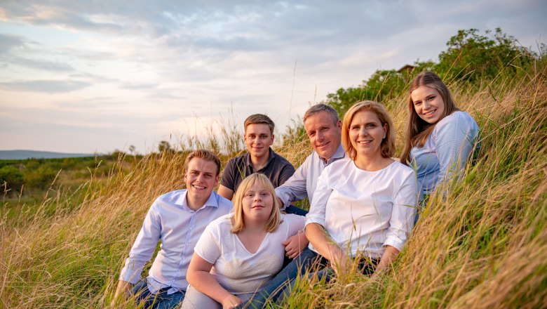 A group of six people sit in a field at sunset.