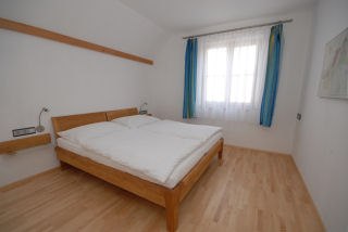 A simply furnished bedroom with a double bed, wooden floor and a window with blue curtains.