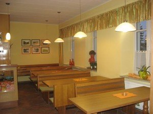 Interior view of a cozy café with wooden tables and benches, decorated with pictures and plants.