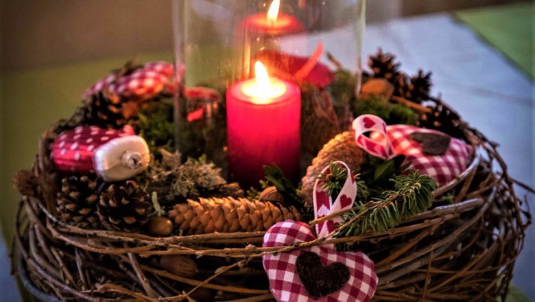 An Advent wreath with a burning red candle, pine cones and red and white checkered fabric hearts.