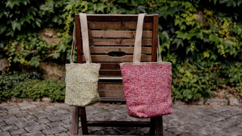 Two handmade bags on a wooden chair in front of a green hedge.