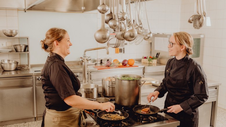 Two cooks in a professional kitchen working at a stove.