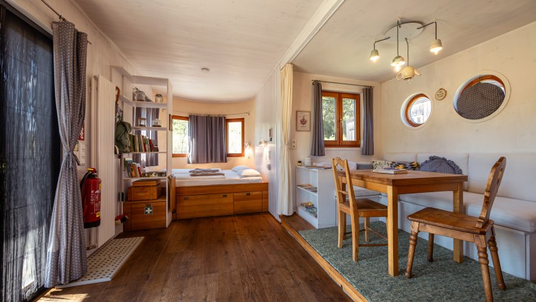Interior view of a cozy country loft with wooden floor, dining table, chairs, bed and shelves.