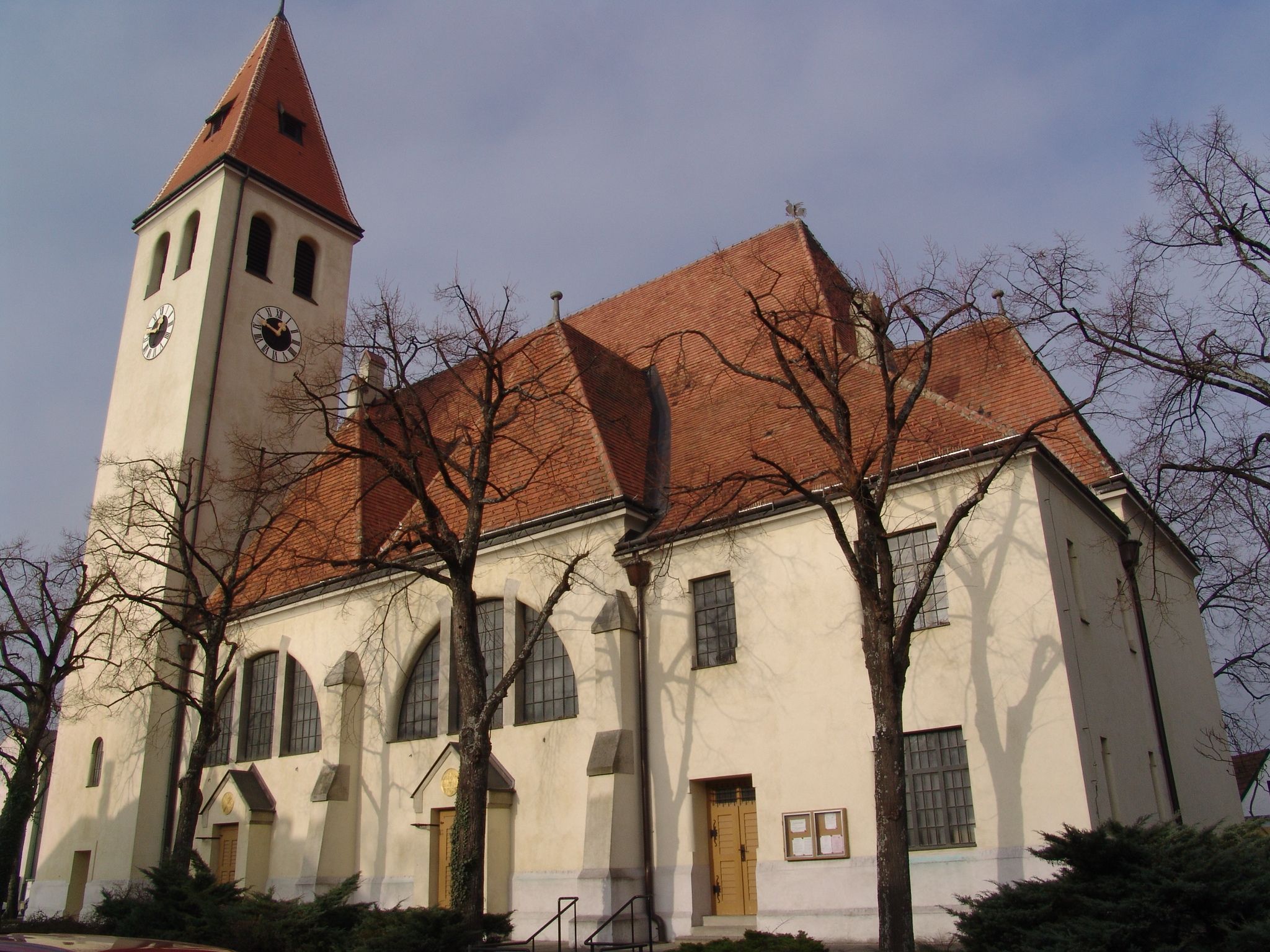 Church with tower and red tiled roof, surrounded by bare trees.