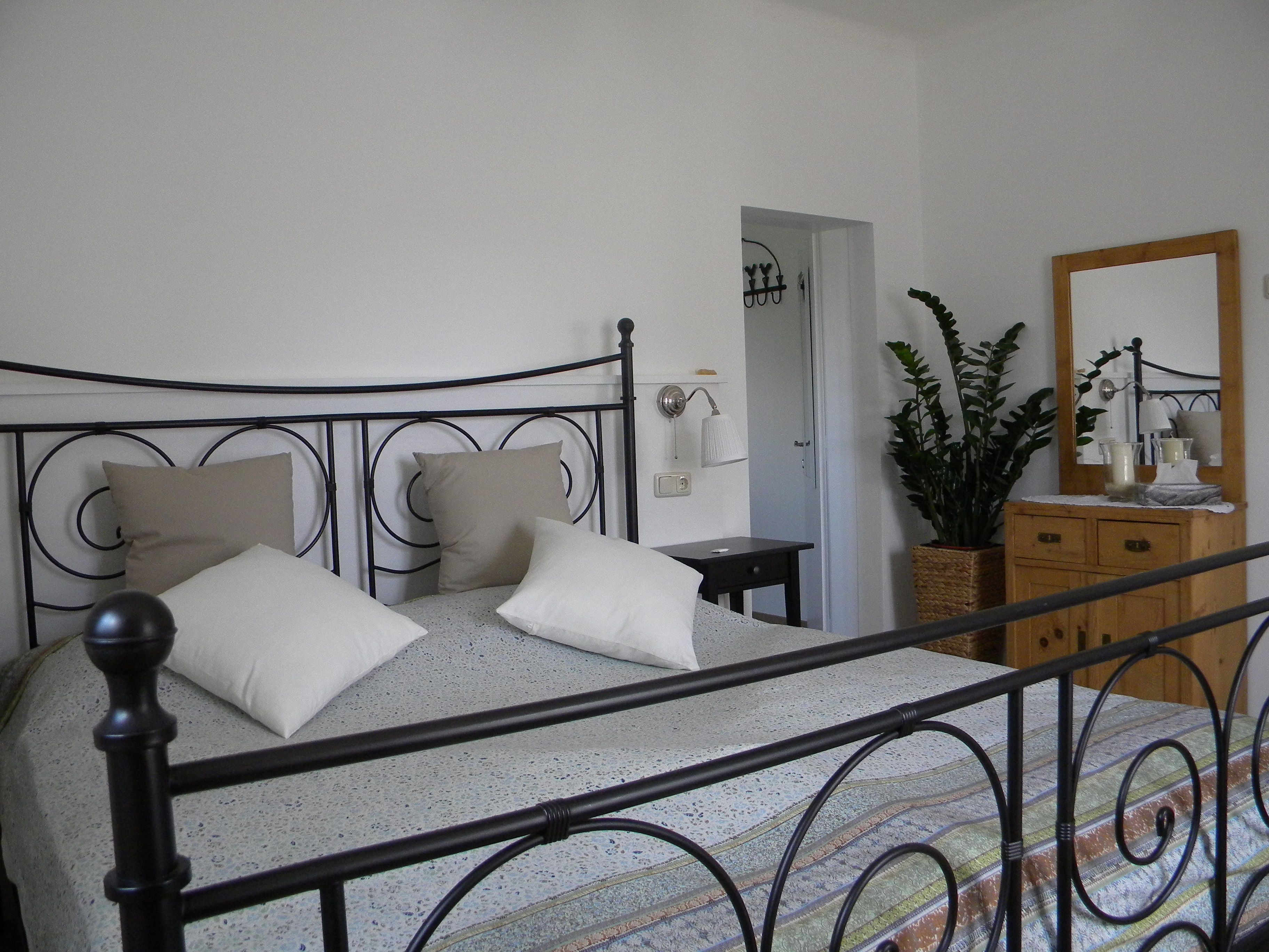 Bedroom with metal bed, chest of drawers and plant.
