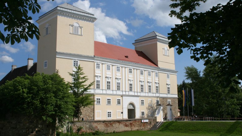 Wolkersdorf Castle with two towers and a red roof, surrounded by trees.