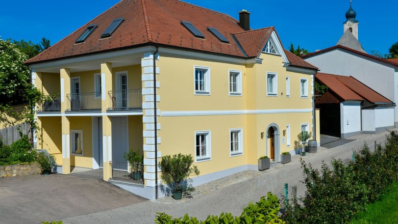 Yellow two-storey house with red roof and balcony, next to it a church with an onion dome.