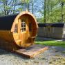 Two wooden barrel huts in a green park with trees.