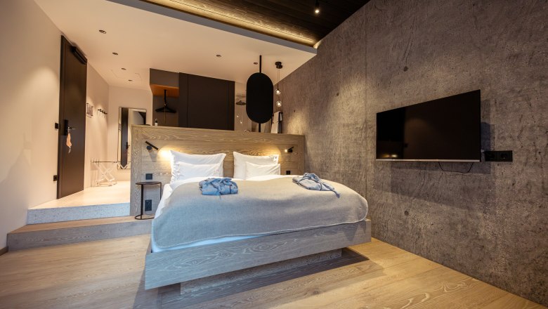 Modern bedroom with wooden floor, gray wall, double bed and flat screen TV.