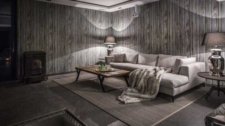 Cozy room with grey sofa, wooden table, fireplace and wood paneling.