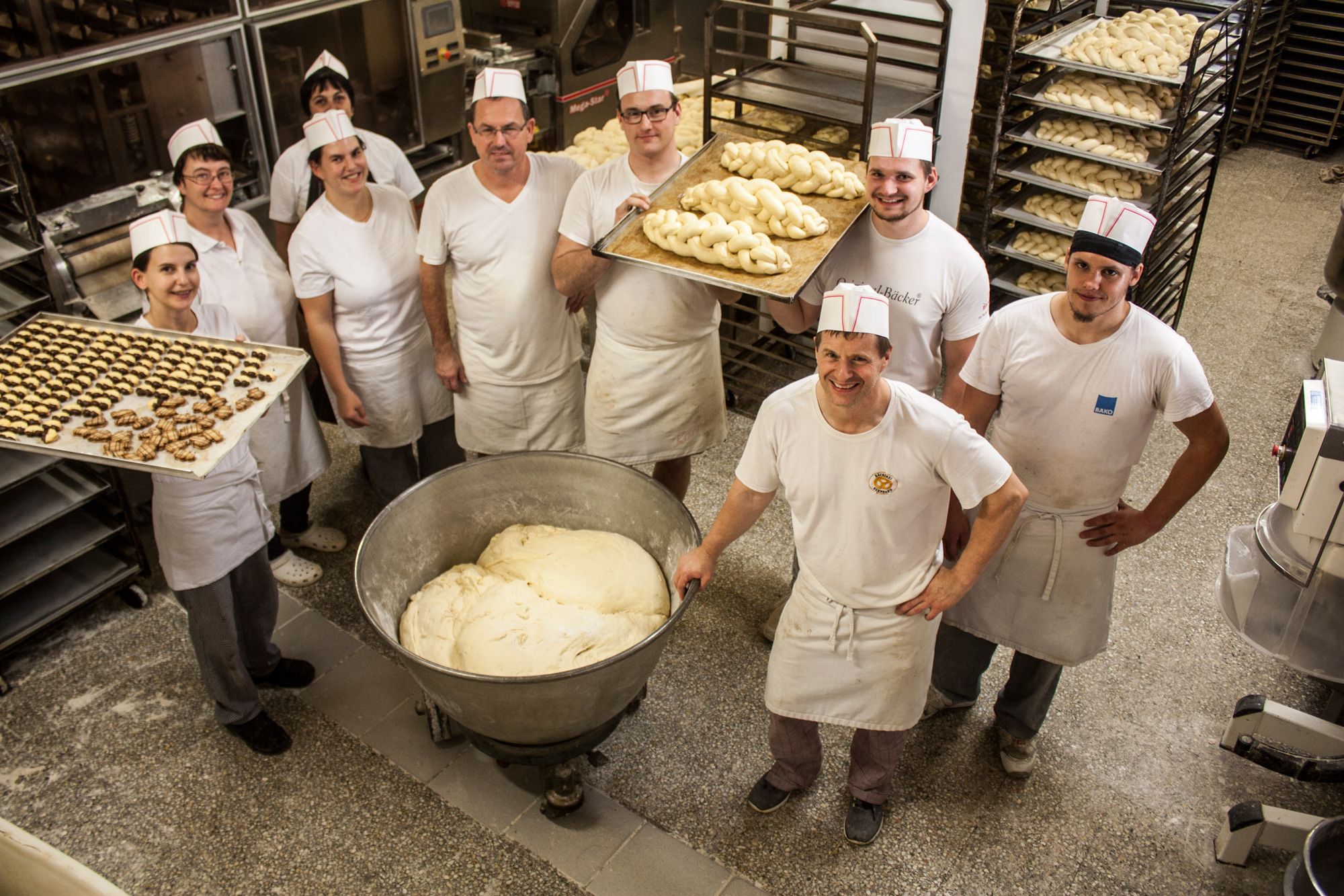 Employees of a bakery in white work clothes with trays full of pasta in a bakery.